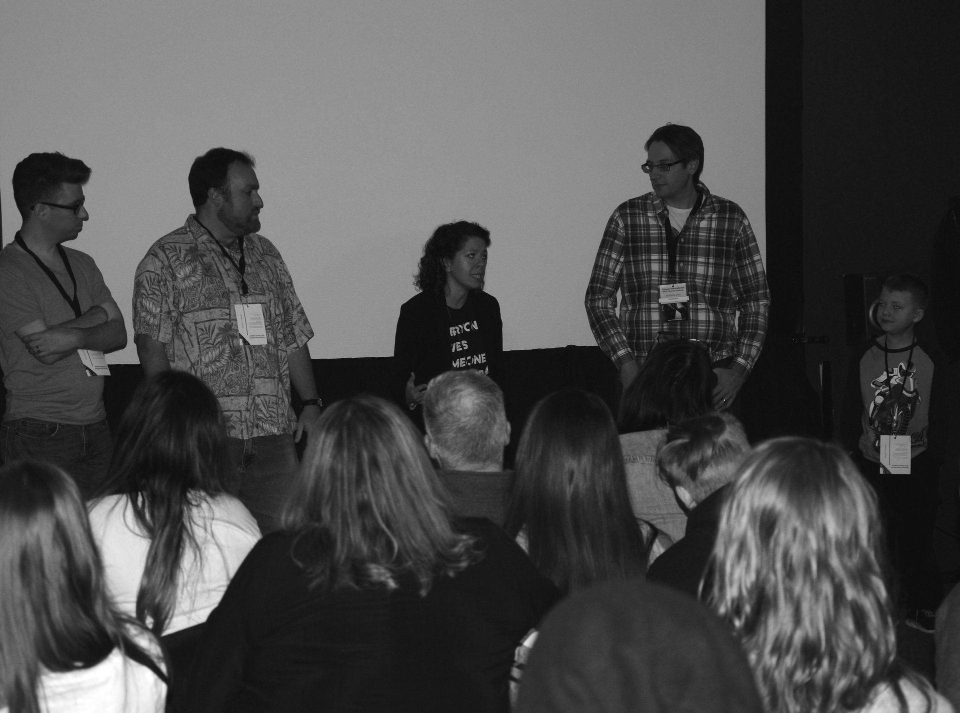 Panel of five people standing before an audience, giving a presentation. Black and white photograph.