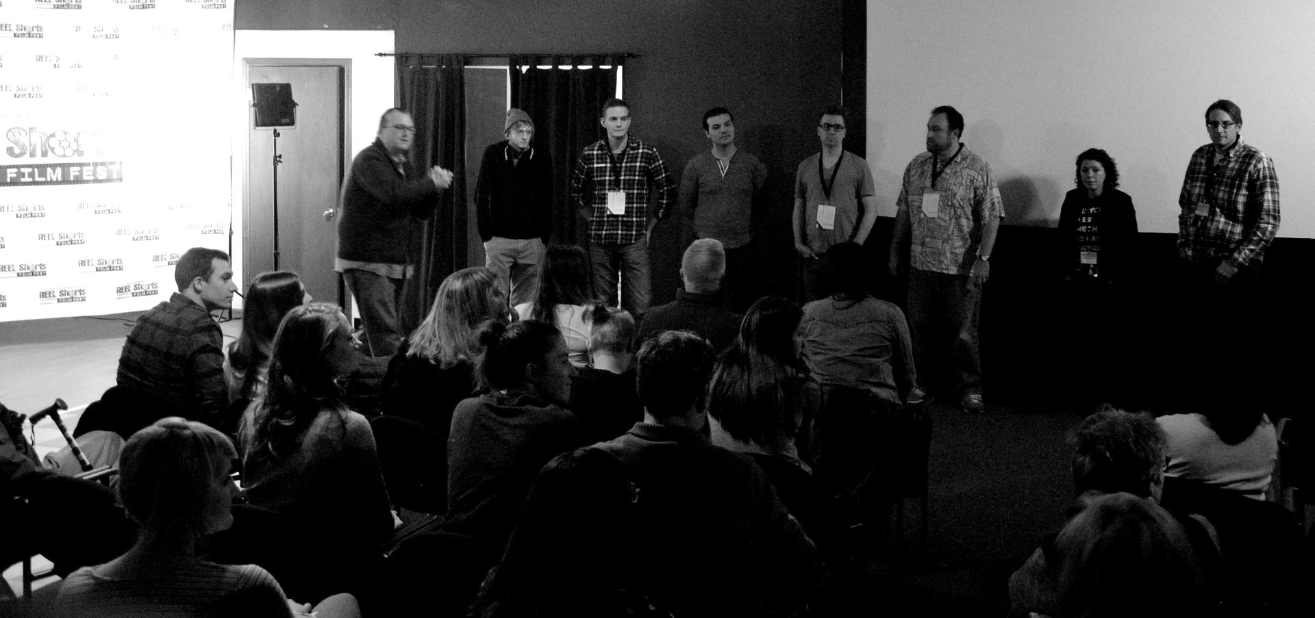 A panel of speakers stands before an audience at a conference or event.
