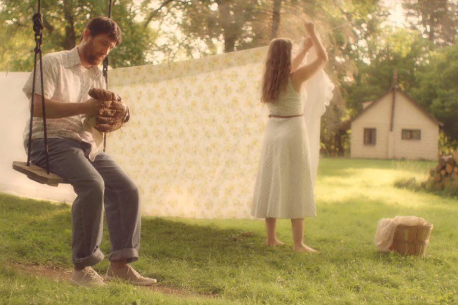 Man on swing, woman hanging laundry in sunlit backyard.
