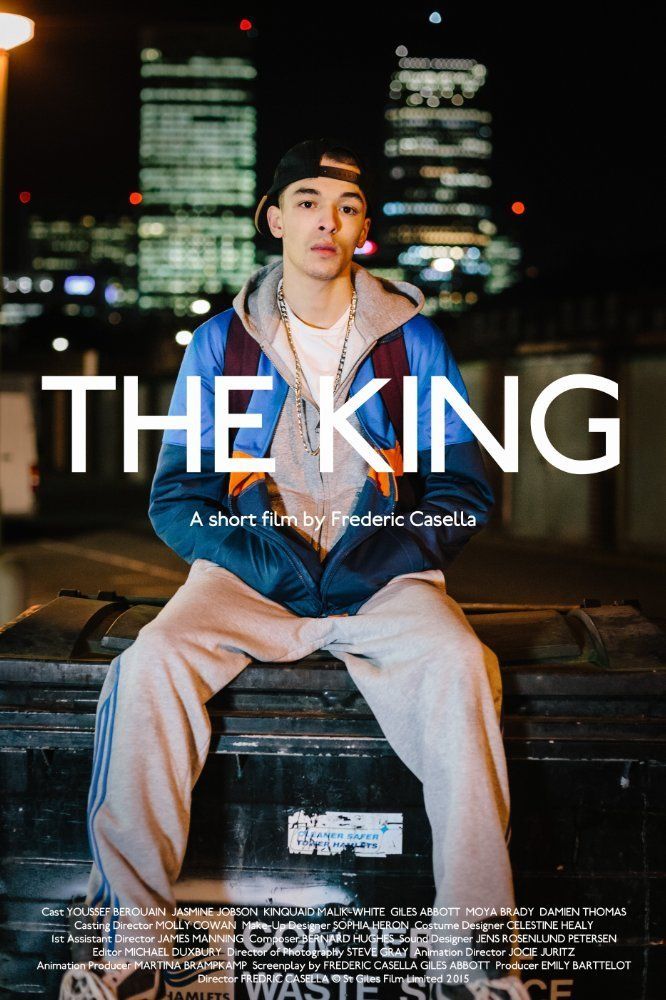 A young man in a blue jacket and cap sits on a trash bin at night in front of a city skyline.