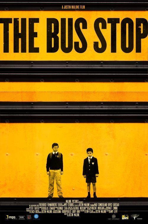 Two young boys in school uniforms stand in front of a yellow school bus.