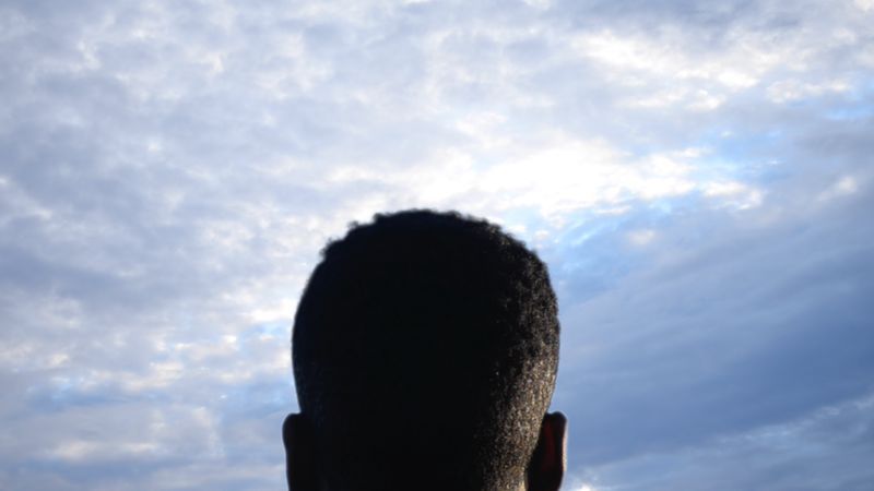 Silhouette of a person's head against a cloudy sky.