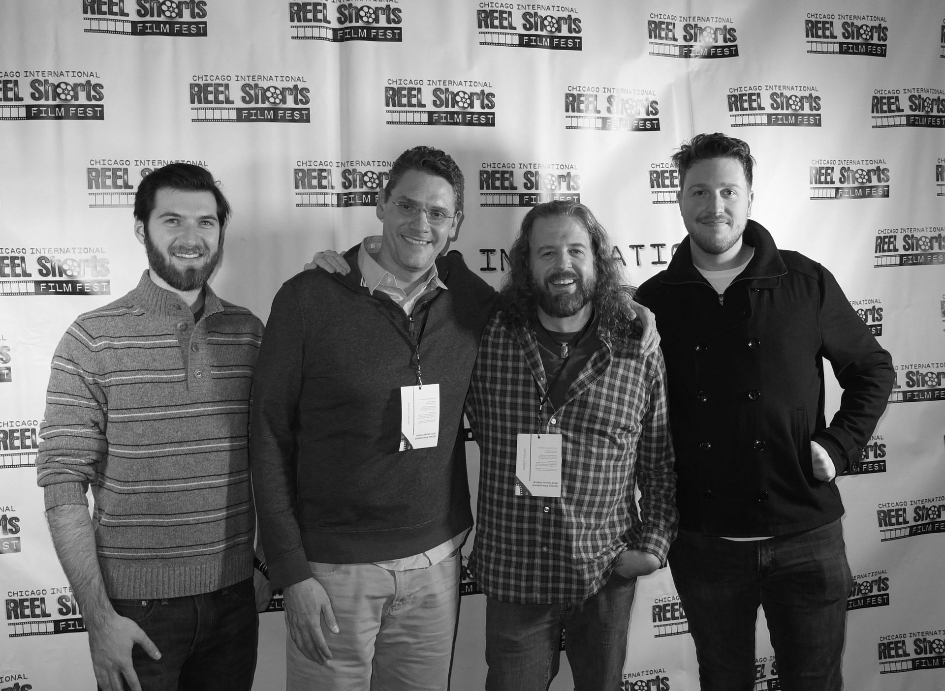 Four men pose smiling in front of a 