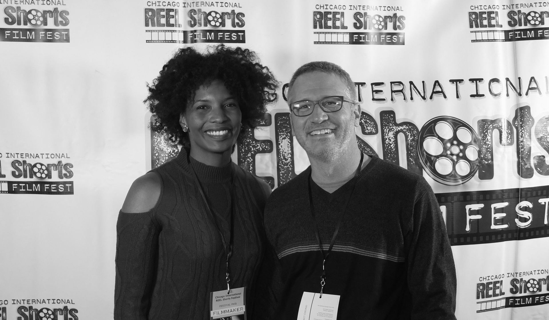 Two people smiling at a film festival event. A woman and a man, in front of a backdrop.