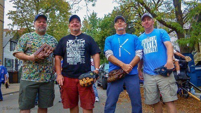 Four men in casual attire holding baseball gloves, standing in a tree-lined street.