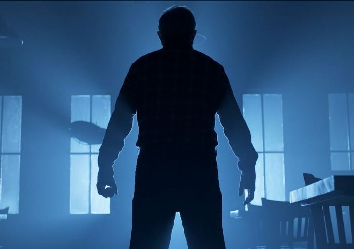 Silhouette of a man in a room with windows, lit by blue light.
