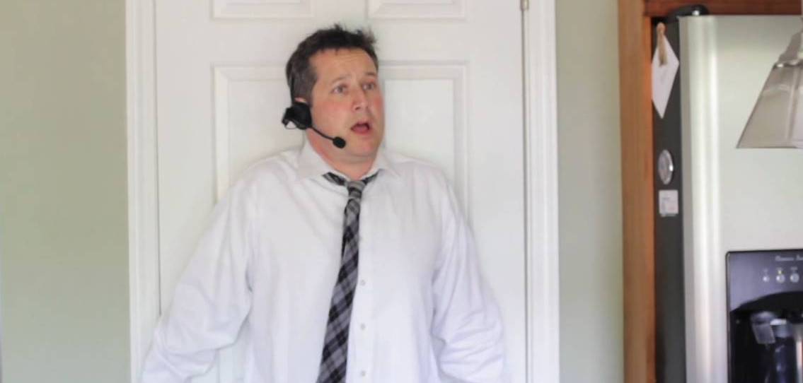 Man in a headset, surprised, standing near a door. He wears a white shirt and tie in a home setting.