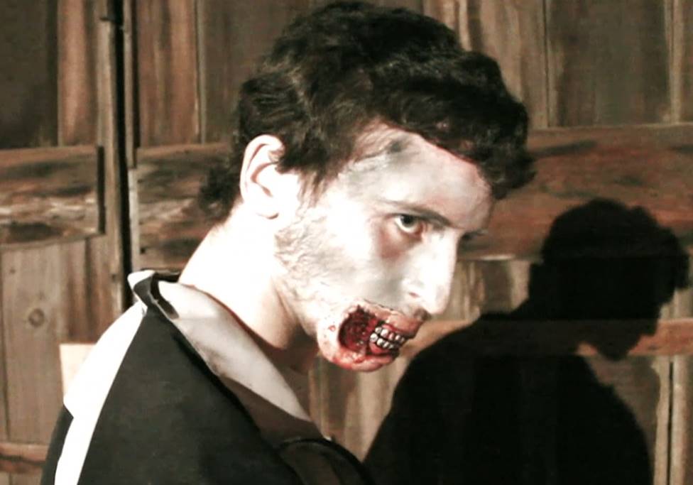 Zombie with bloody mouth, pale skin, dark hair, staring with an angry expression. Set against a wood background.