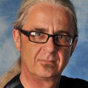 Man with gray hair pulled back, wearing glasses, looking at the camera with a neutral expression.