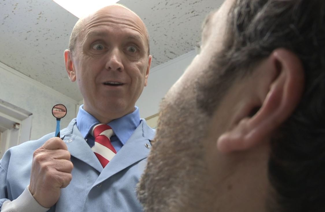 Bald dentist with wide eyes and mirror examining a patient's ear.
