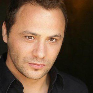 Man with brown eyes, dark hair, wearing a black shirt, looking at the camera.