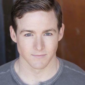 Young man with fair skin and blue eyes smiles.