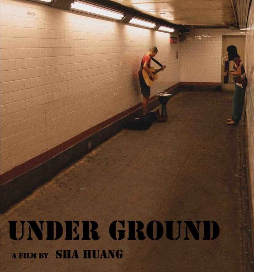 A musician plays guitar in a subway tunnel. Another person stands nearby. The film title 