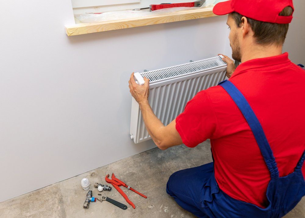 Plumber Installing Heating Radiator — Irwin, PA — Westmoreland Affordable Plumbing Heating & Cooling Plumber Installing Heating Radiator — Irwin, PA — Westmoreland Affordable Plumbing Heating & Cooling