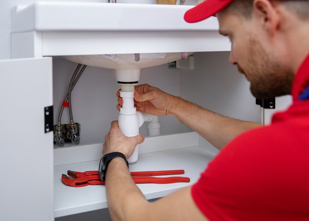 Plumber Installing Sink Siphon in Domestic Bathroom — Irwin, PA — Westmoreland Affordable Plumbing Heating & Cooling Plumber Installing Sink Siphon in Domestic Bathroom — Irwin, PA — Westmoreland Affordable Plumbing Heating & Cooling