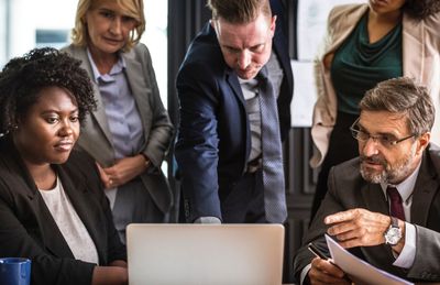 The Firm IR Group can help with everything from special projects to PowerPoint creation and more. Image is of a group of business people gathered around a computer.