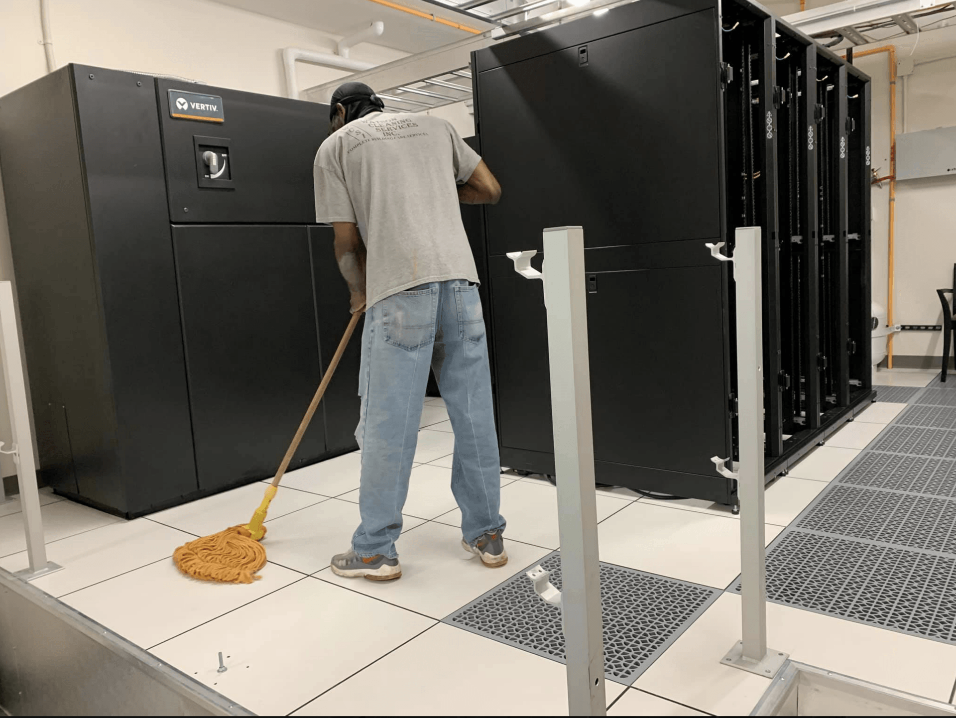 Person sweeping floor between large black server racks in a data center.