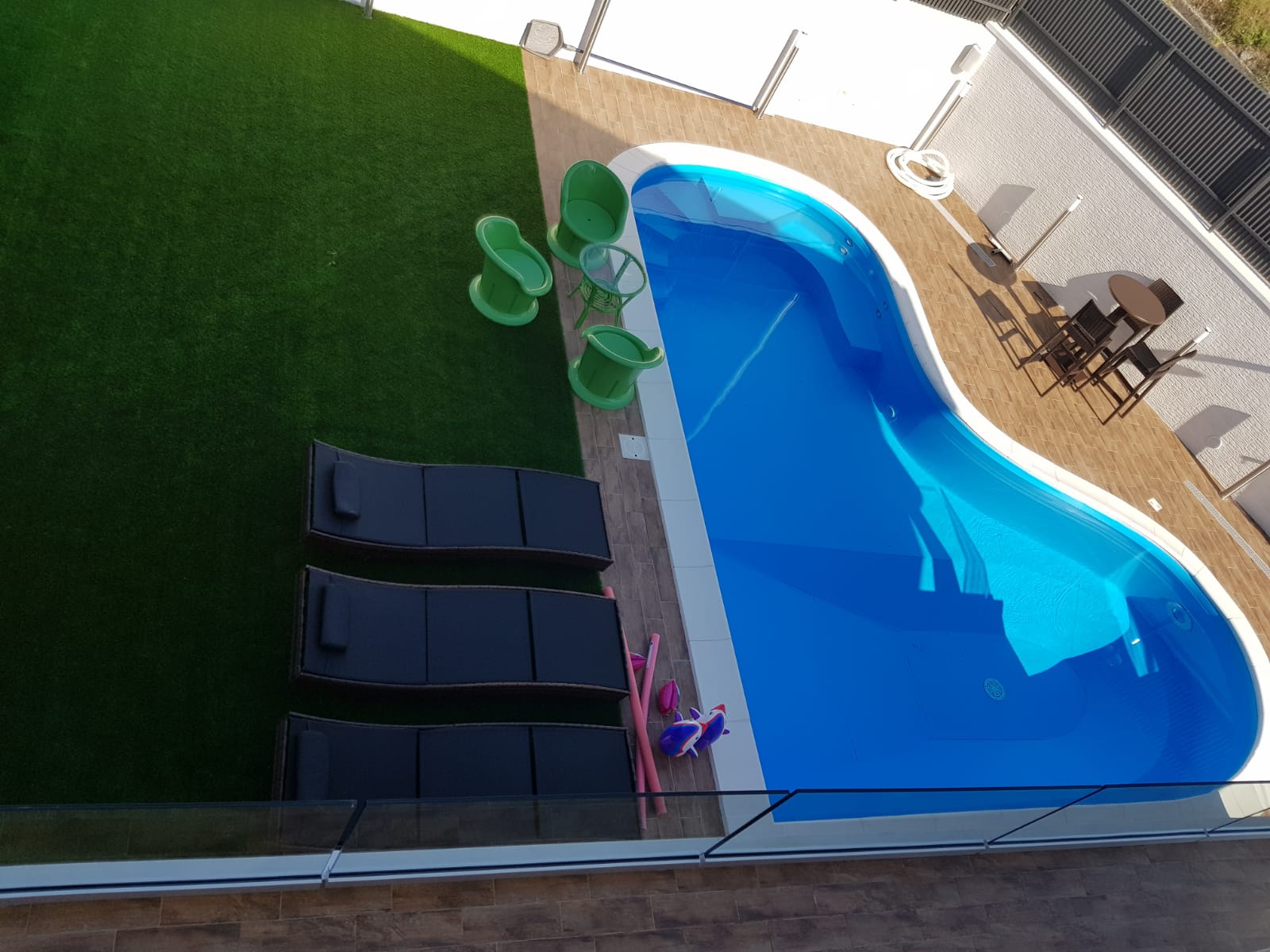Vista dall'alto di una piscina con chaise longue, erba artificiale e zona pranzo.