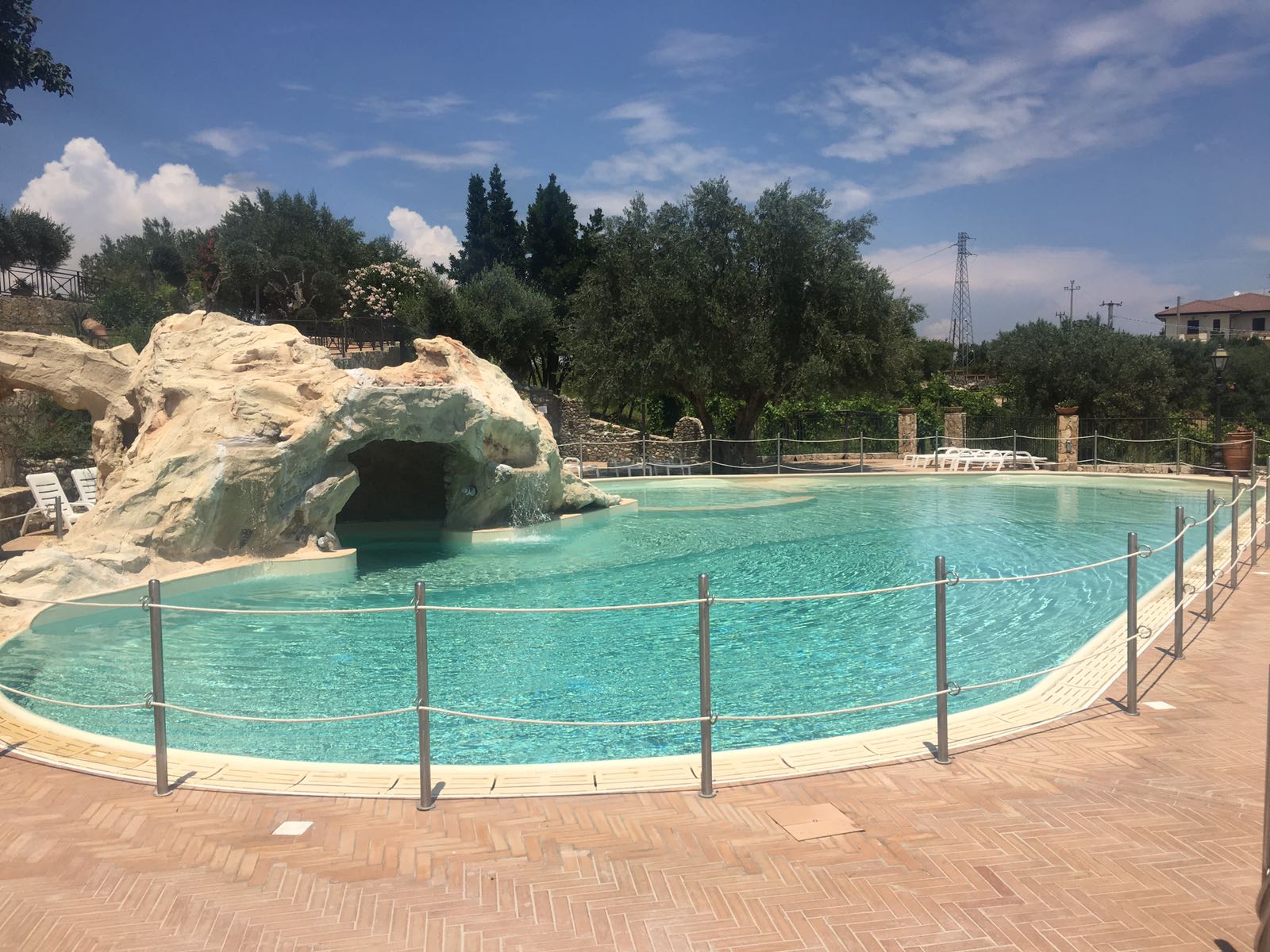 Piscina con acqua turchese circondata da una formazione rocciosa di colore chiaro e alberi sotto un cielo azzurro.