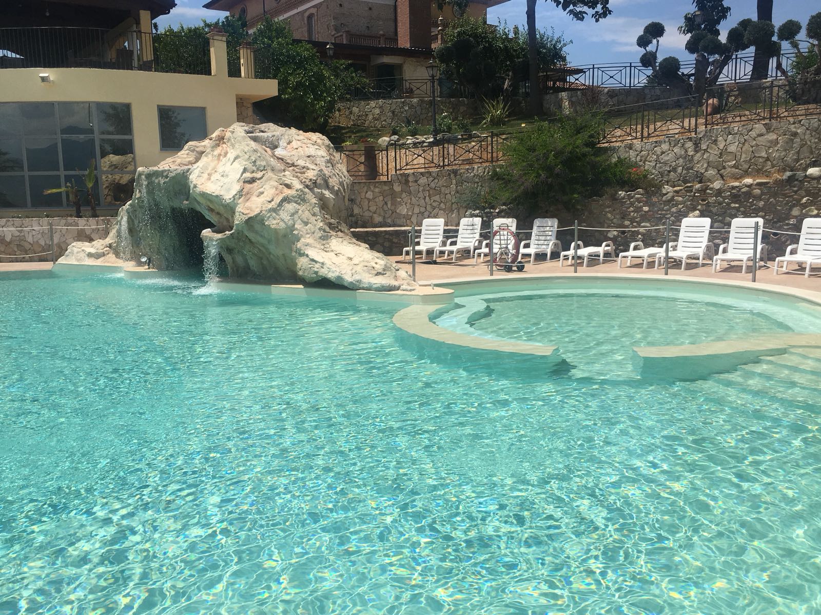 Piscina con cascata e sedie a sdraio.