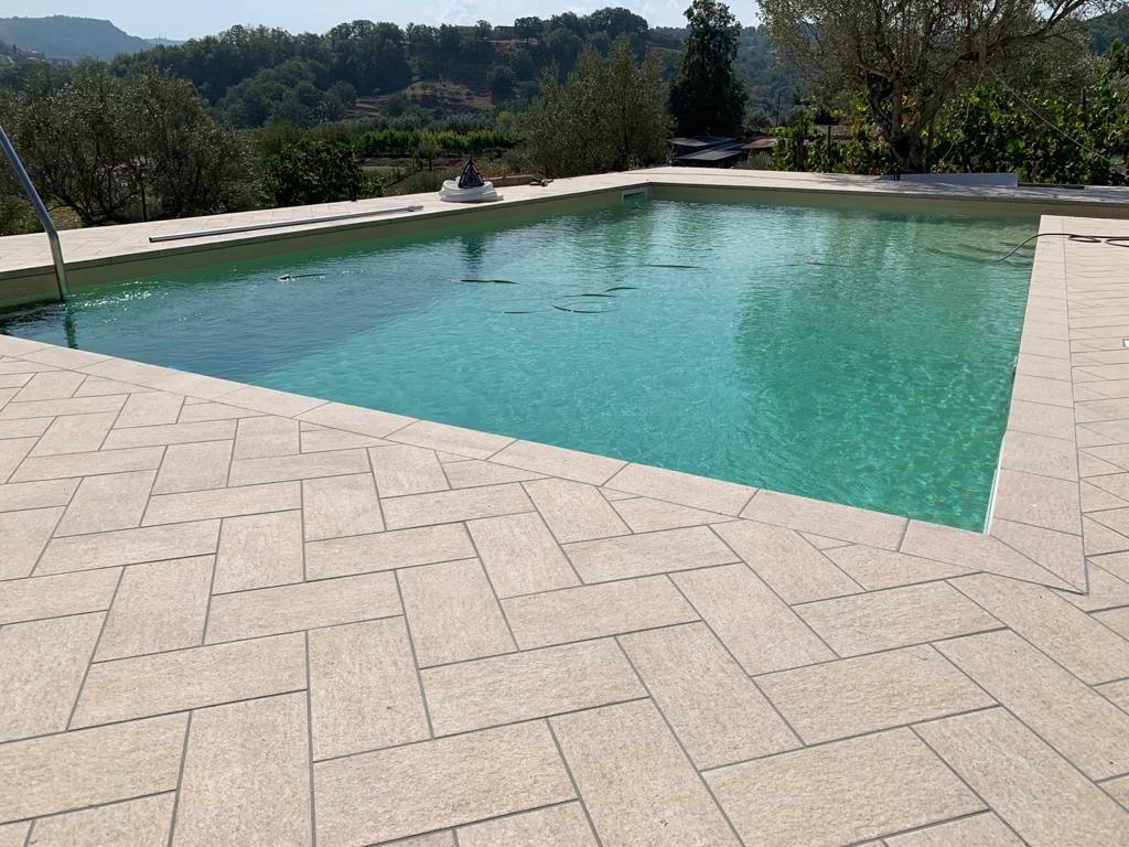 Piscina con acqua turchese, circondata da pietre chiare, con vista su un paesaggio collinare.