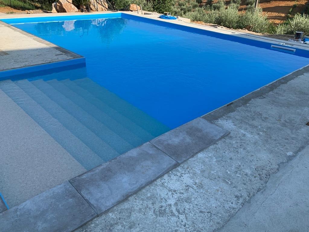 Piscina blu con gradini, circondata da cemento e verde.