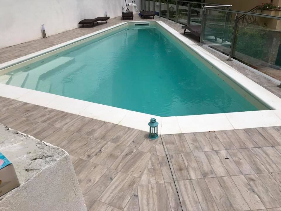 Piscina con finiture bianche e terrazza in legno. Acqua turchese.