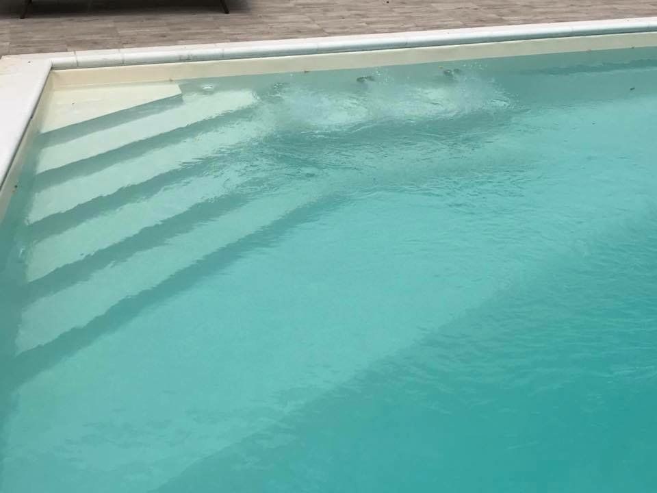 Piscina turchese trasparente con scale interne. Le bollicine salgono dall'acqua.