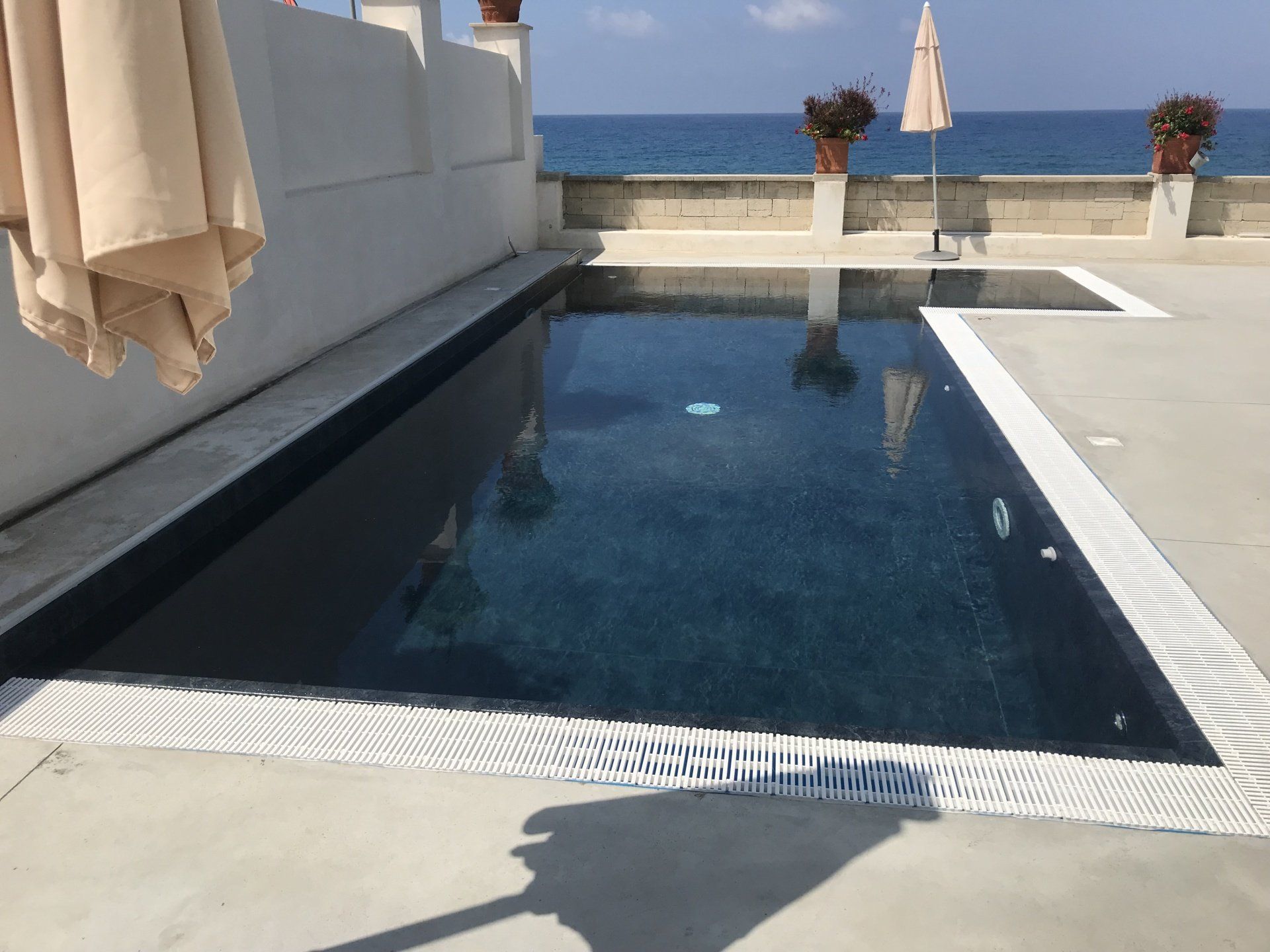 Piscina su un ponte con vista sull'oceano, dotata di ombrellone e piante in vaso.