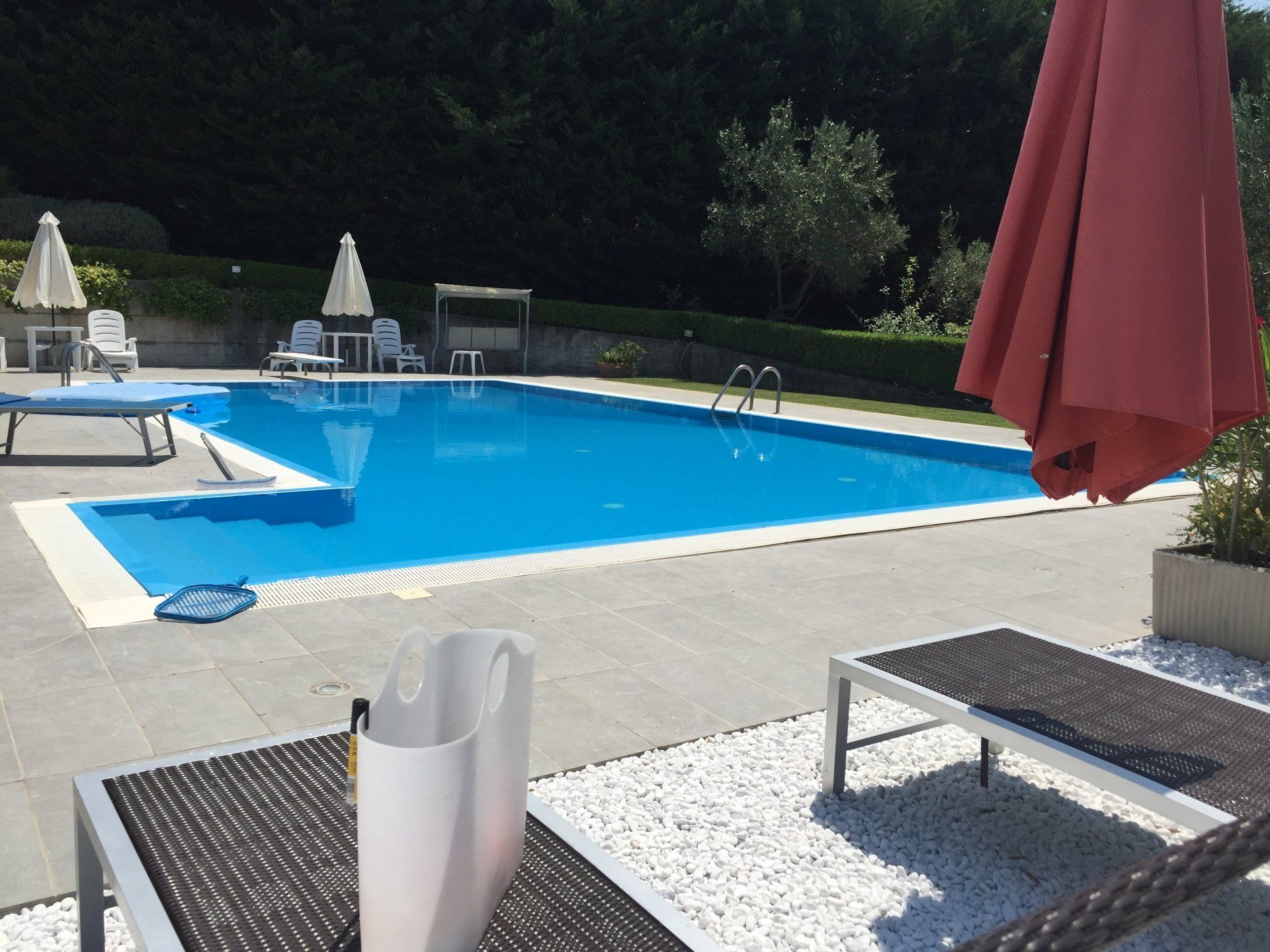 Piscina con acqua azzurra circondata da patio, sedie a sdraio e ombrelloni.