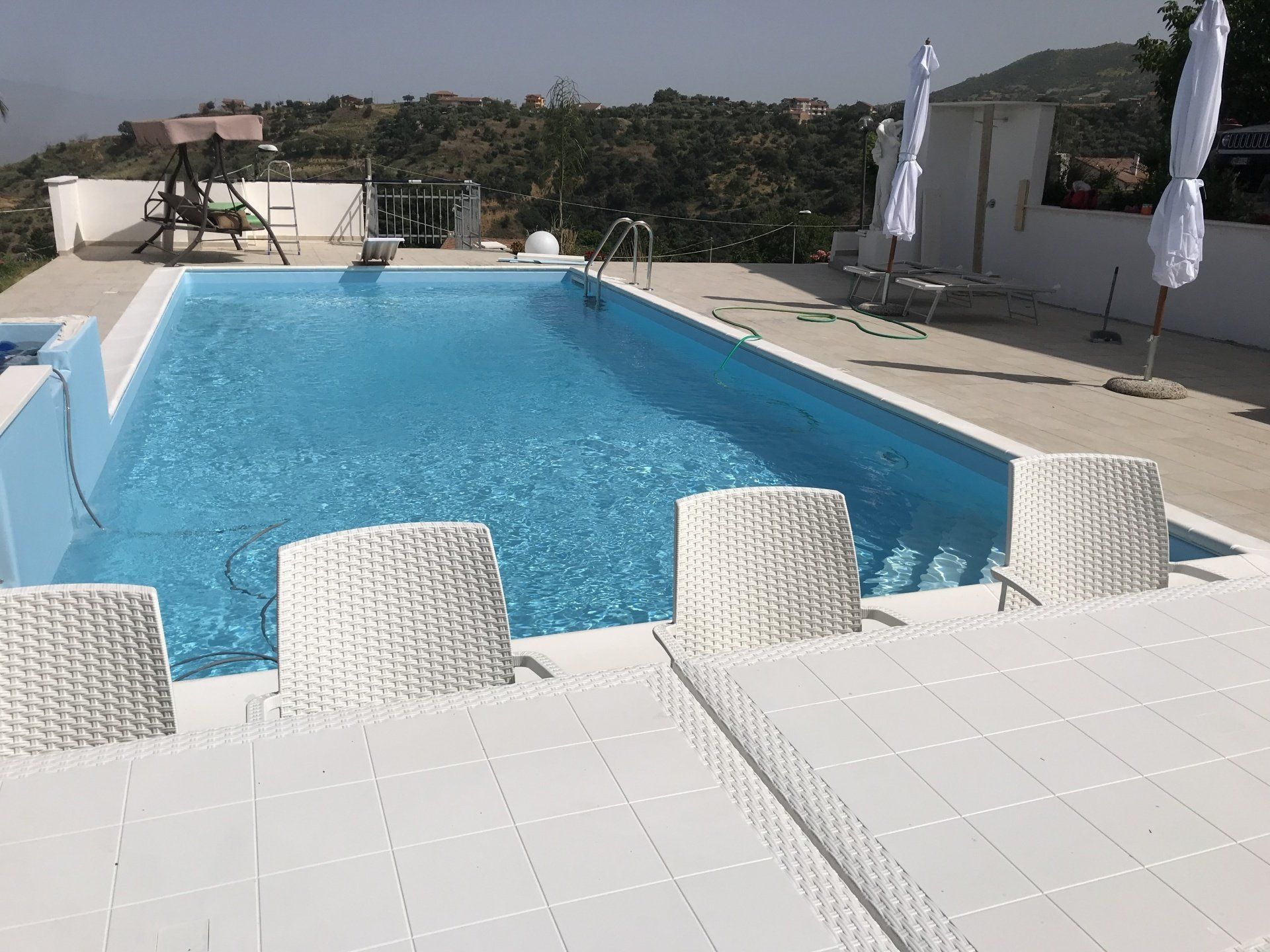 Piscina con mobili da giardino bianchi e ombrelloni, posizione soleggiata all'aperto.