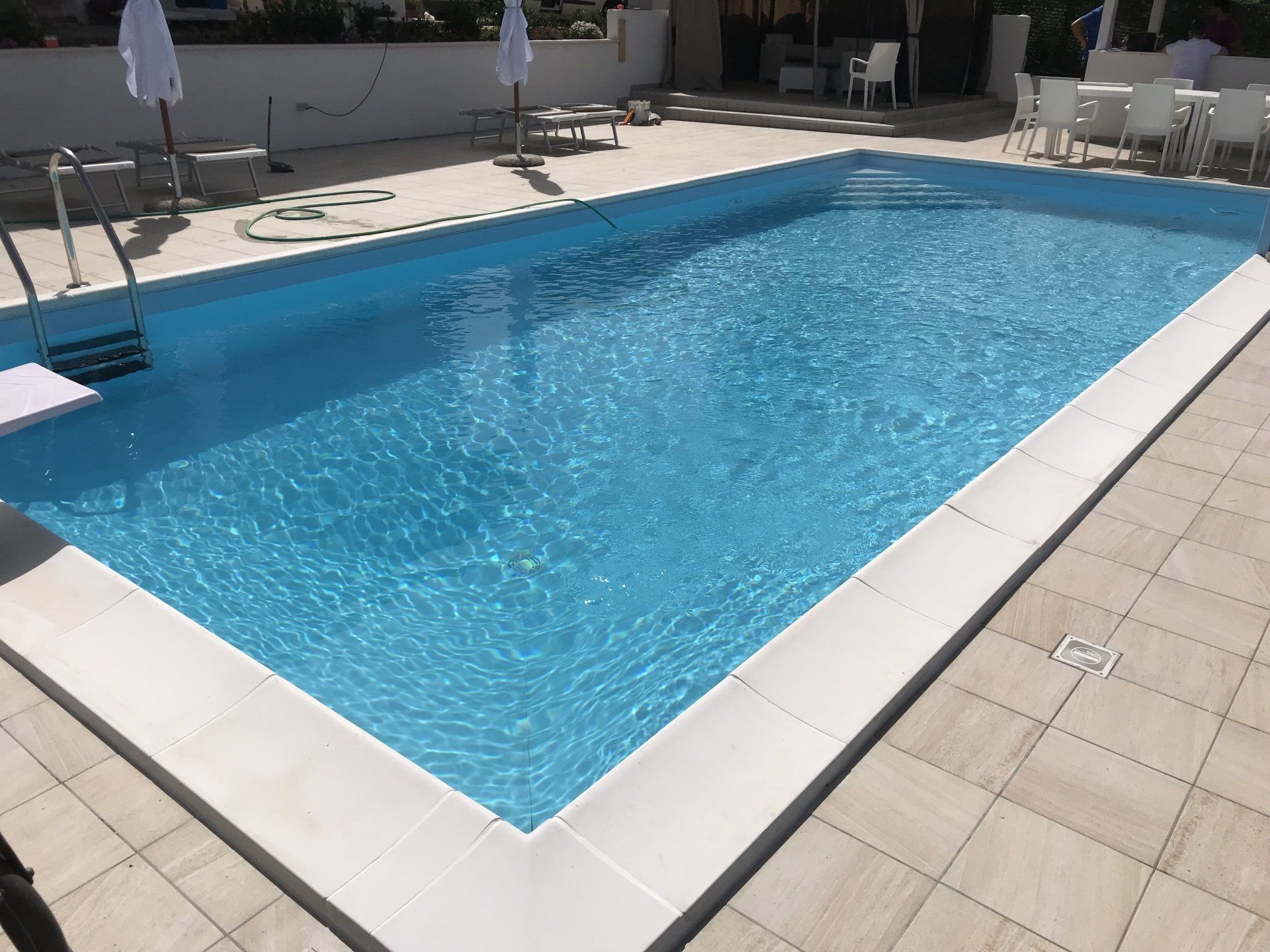 Una piscina rettangolare riempita di acqua turchese, circondata da piastrelle di colore chiaro.