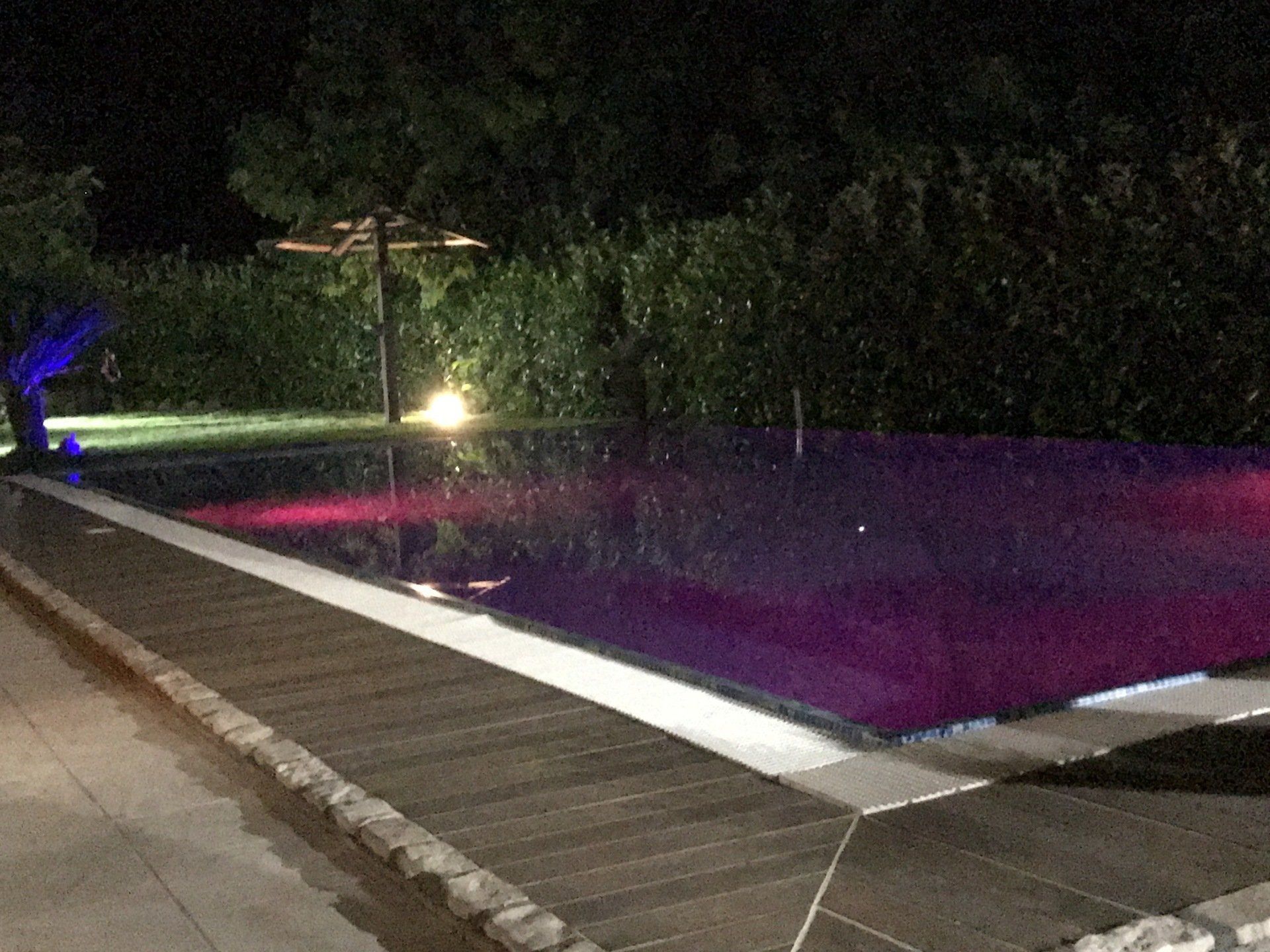 Vista notturna di una piscina rettangolare con luci colorate che si riflettono sull'acqua.