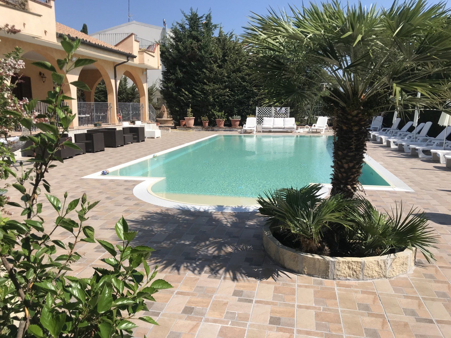 Piscina circondata da patio in pietra, sedie a sdraio e struttura con archi.