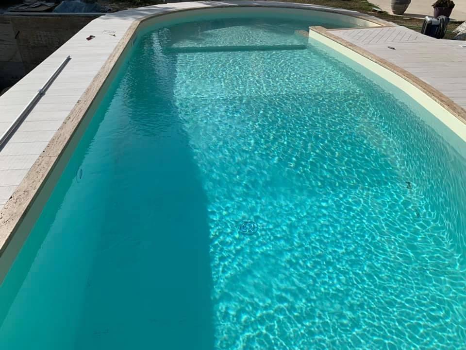 Una piscina turchese con bordo in piastrelle bianche sotto un cielo luminoso.