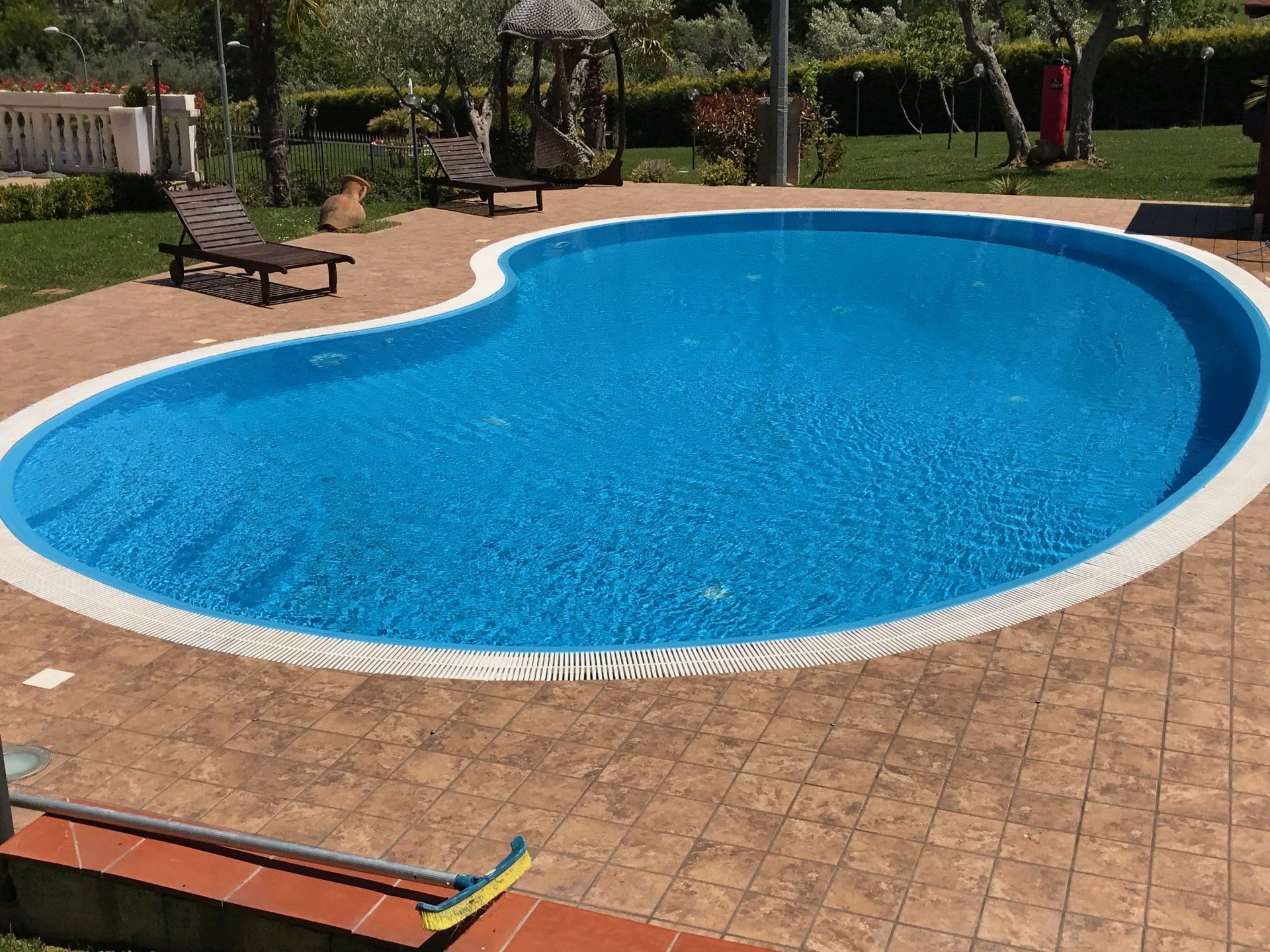 Piscina a forma di rene con piastrelle blu, circondata da un patio in mattoni marroni