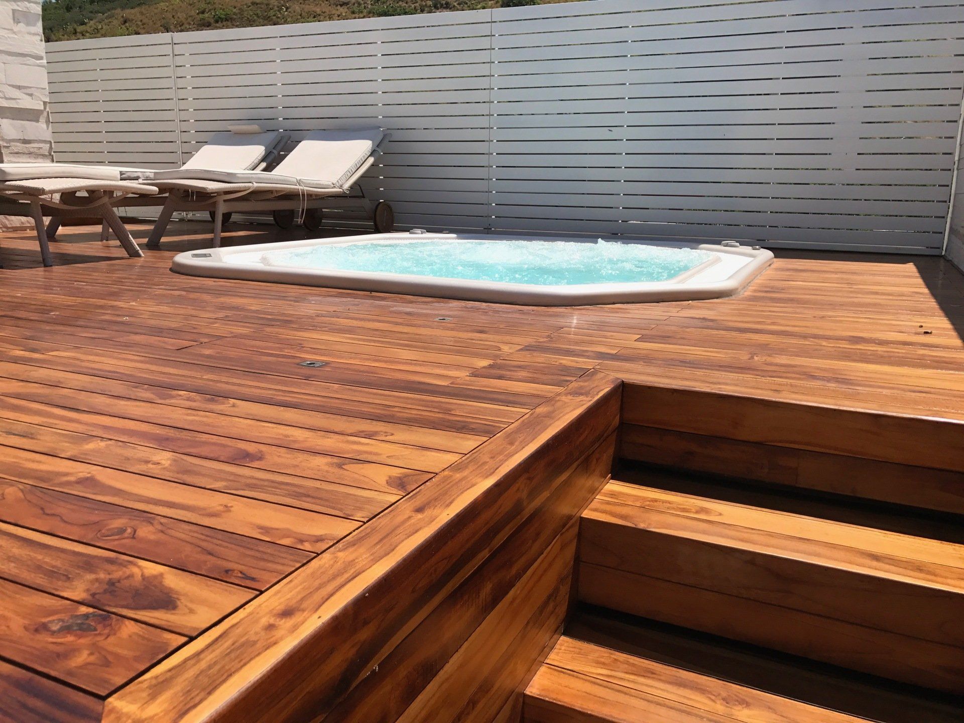 Terrazza in legno con vasca idromassaggio, sedie a sdraio e recinzione bianca decorativa.