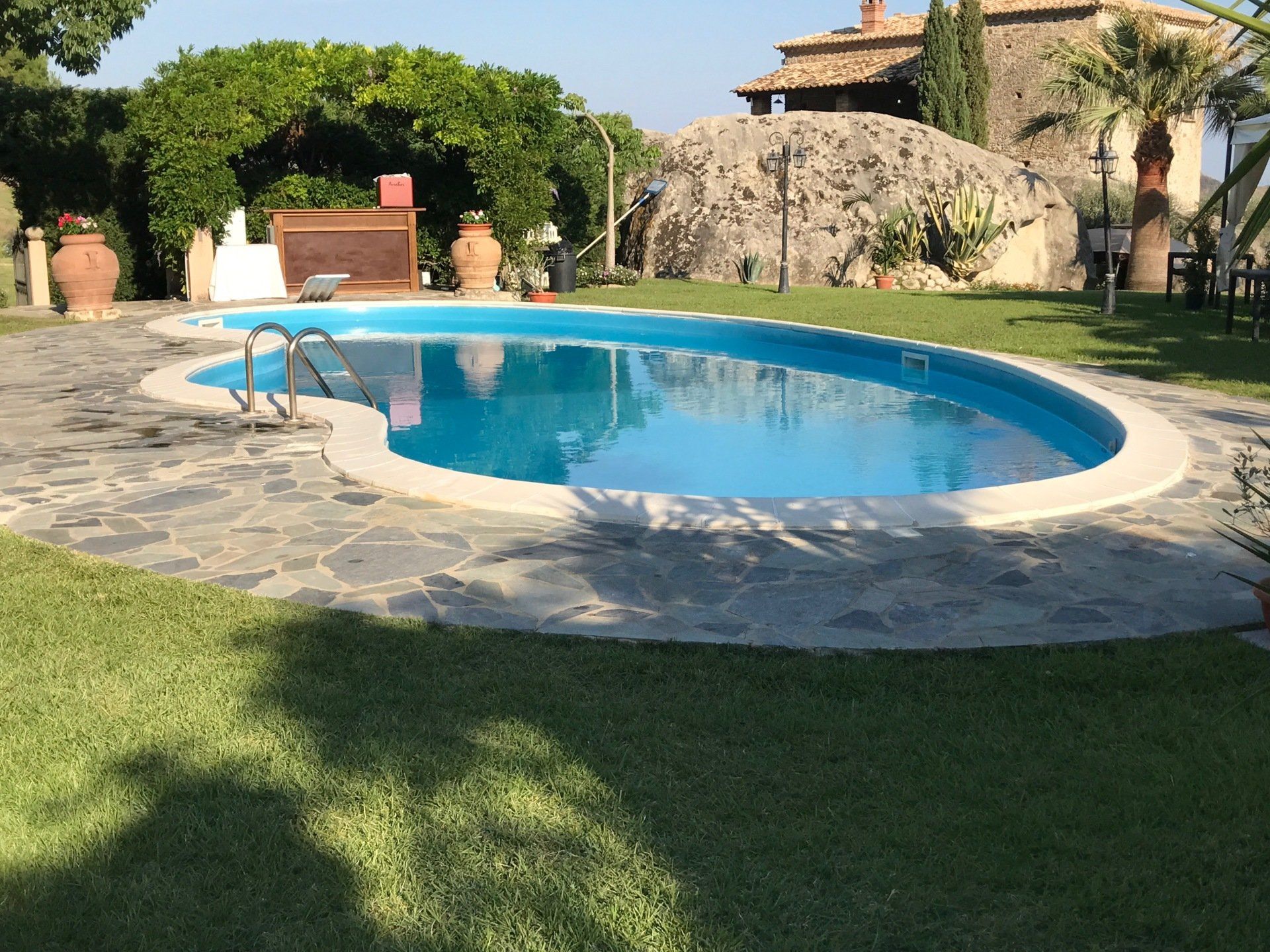 Piscina circondata da prato verde e patio in pietra in un ambiente esterno soleggiato.