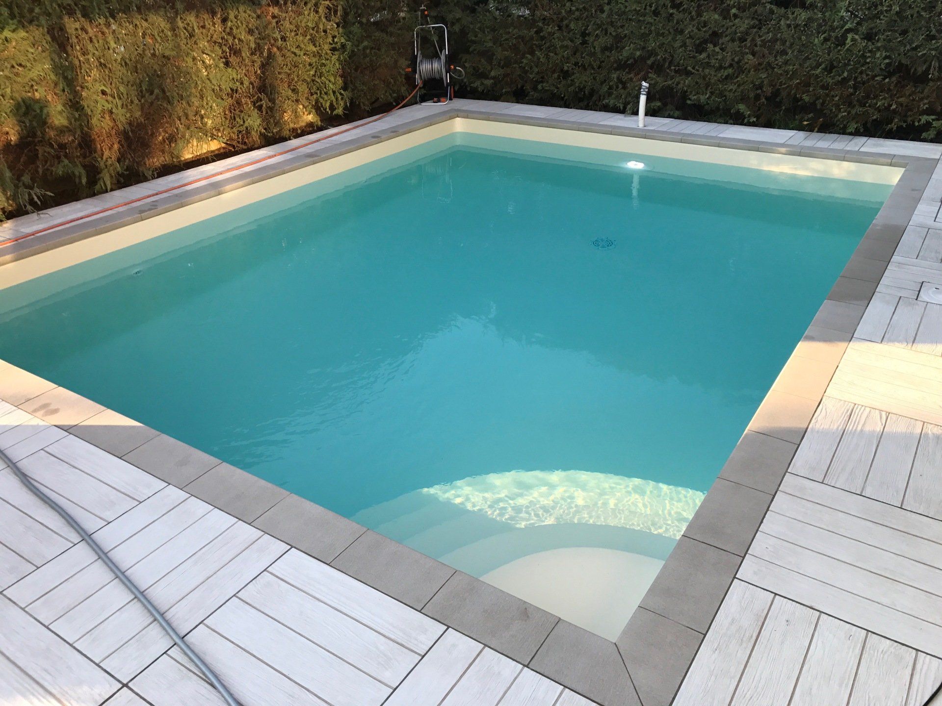 Una piscina rettangolare riempita di acqua turchese, circondata da una terrazza dai colori chiari.