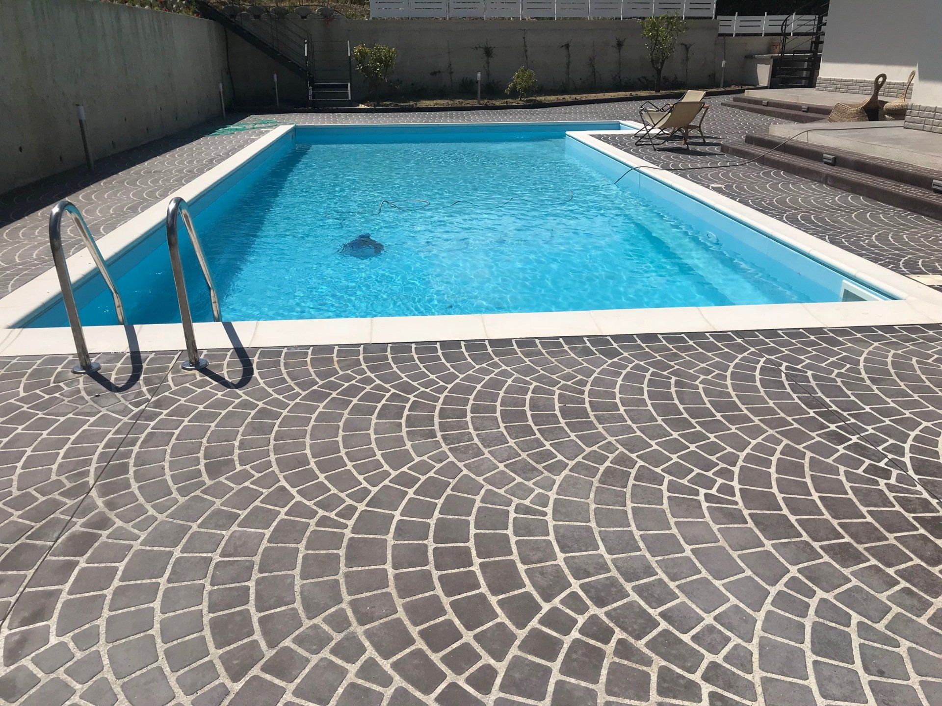 Una piscina rettangolare circondata da ciottoli grigi. La piscina è dotata di scaletta.