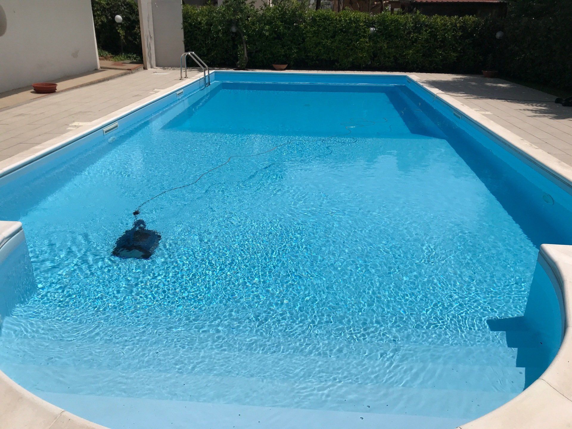 Una piscina rettangolare piena di acqua blu; un pulitore robotico è immerso.