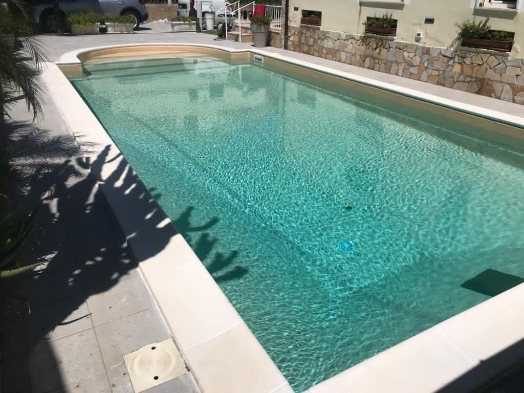 Piscina rettangolare con acqua azzurra e bordo in pietra, all'aperto.