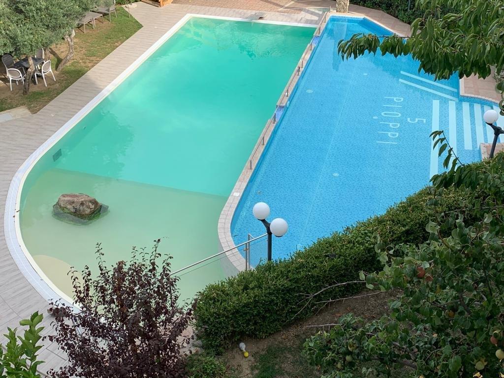 Piscina divisa in due parti: una sezione è verde chiaro, l'altra blu con gradini e un cartello 