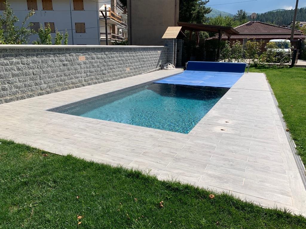 Piscina esterna rettangolare con acqua blu e copertura, circondata da pietra ed erba.