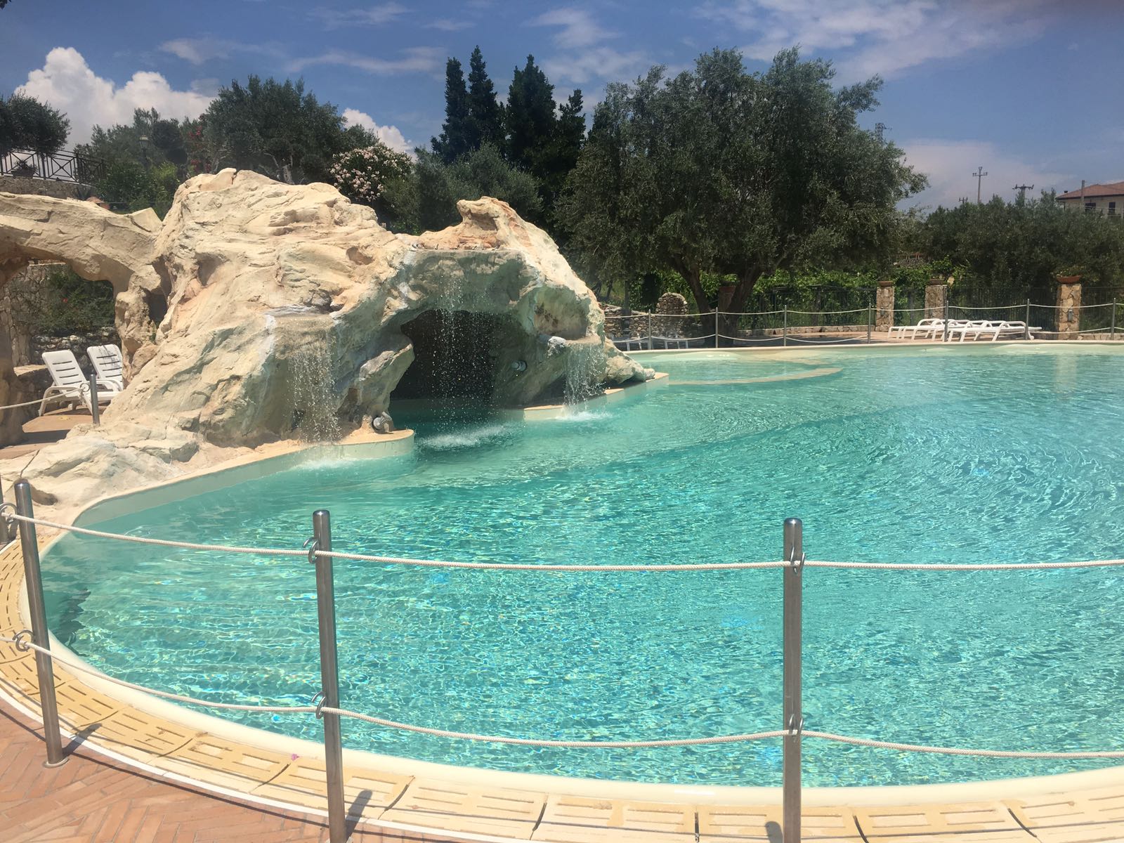 Piscina con cascata formata da rocce, all'esterno soleggiato.
