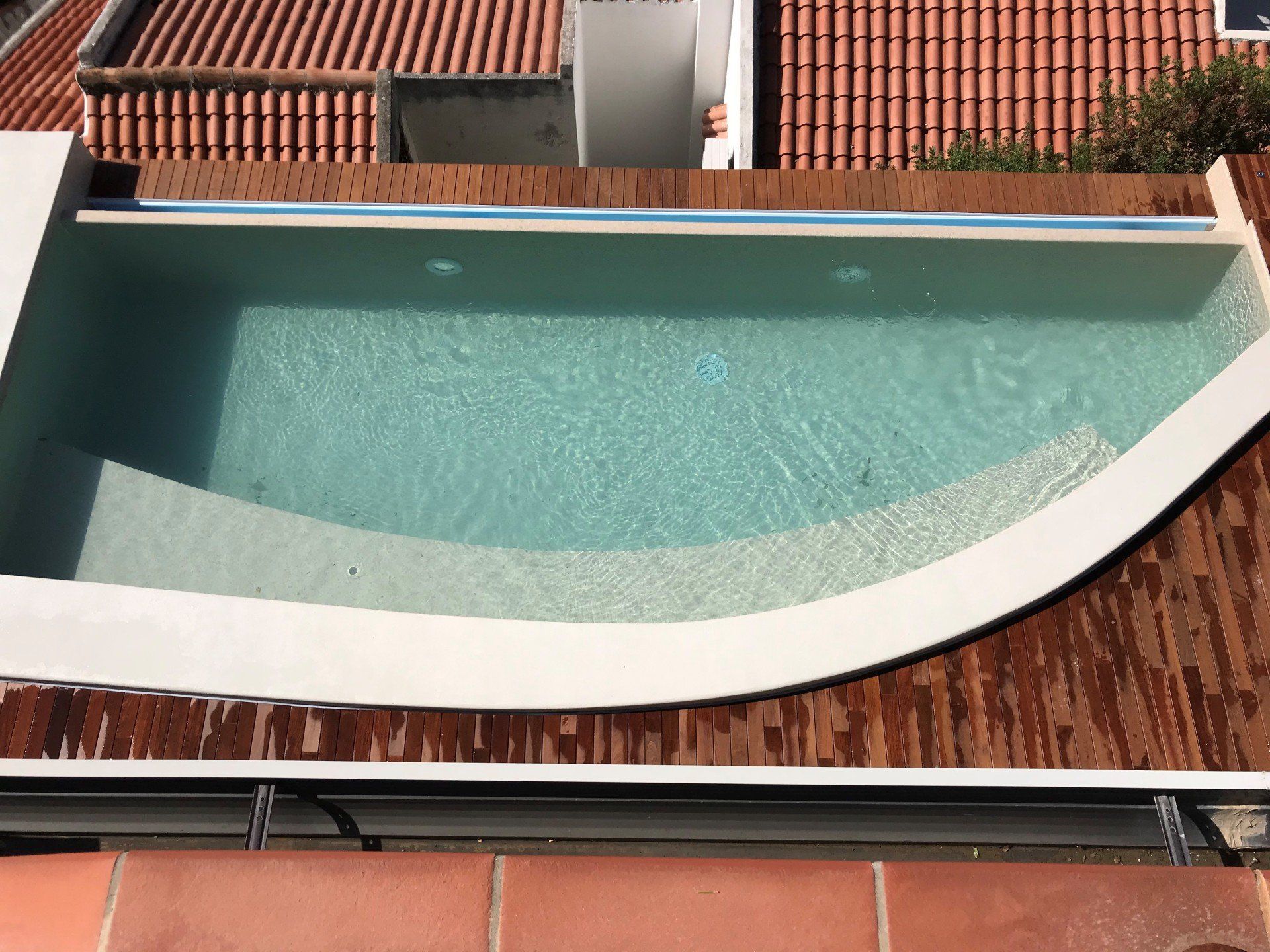 Piccola piscina sul tetto con bordi bianchi, gradini integrati e terrazza in legno marrone.