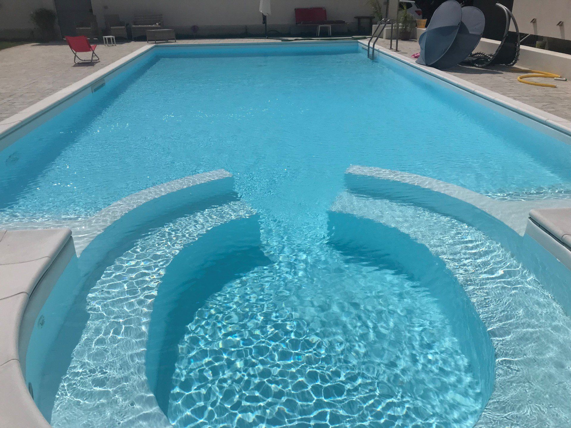 Una piscina rettangolare con una sezione circolare collegata, riempita con acqua blu scintillante.