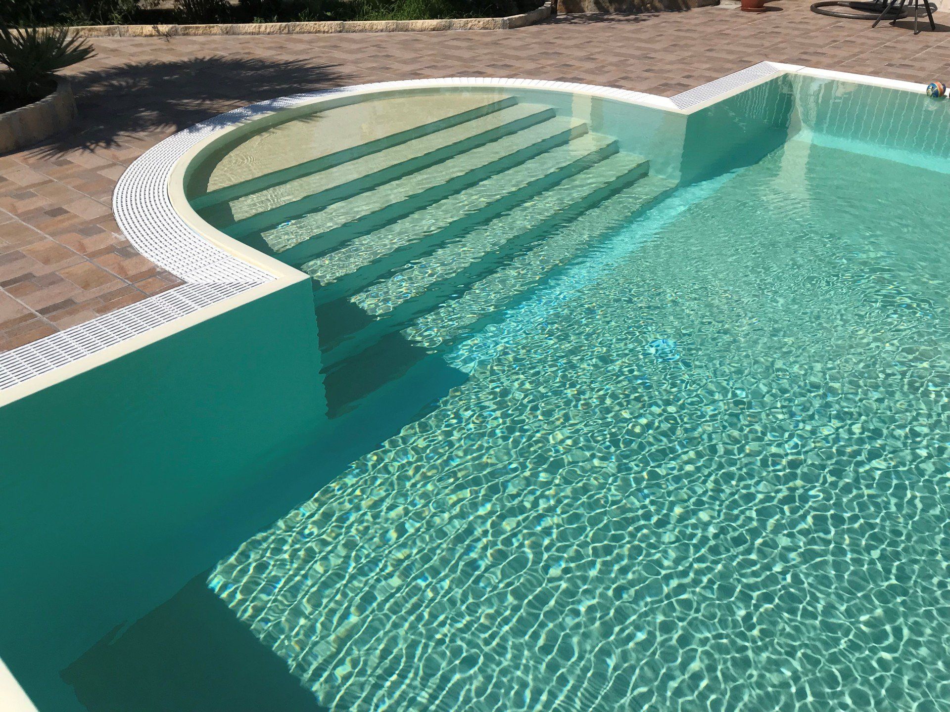 Piscina con gradini sommersi e acqua turchese, bordata di mattoni.
