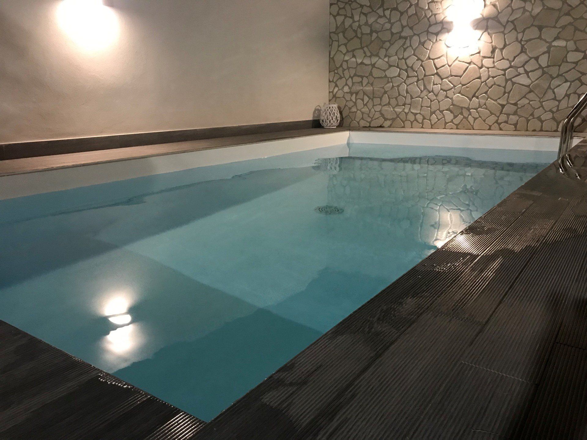Piscina coperta con pavimentazione scura e parete decorativa in pietra.