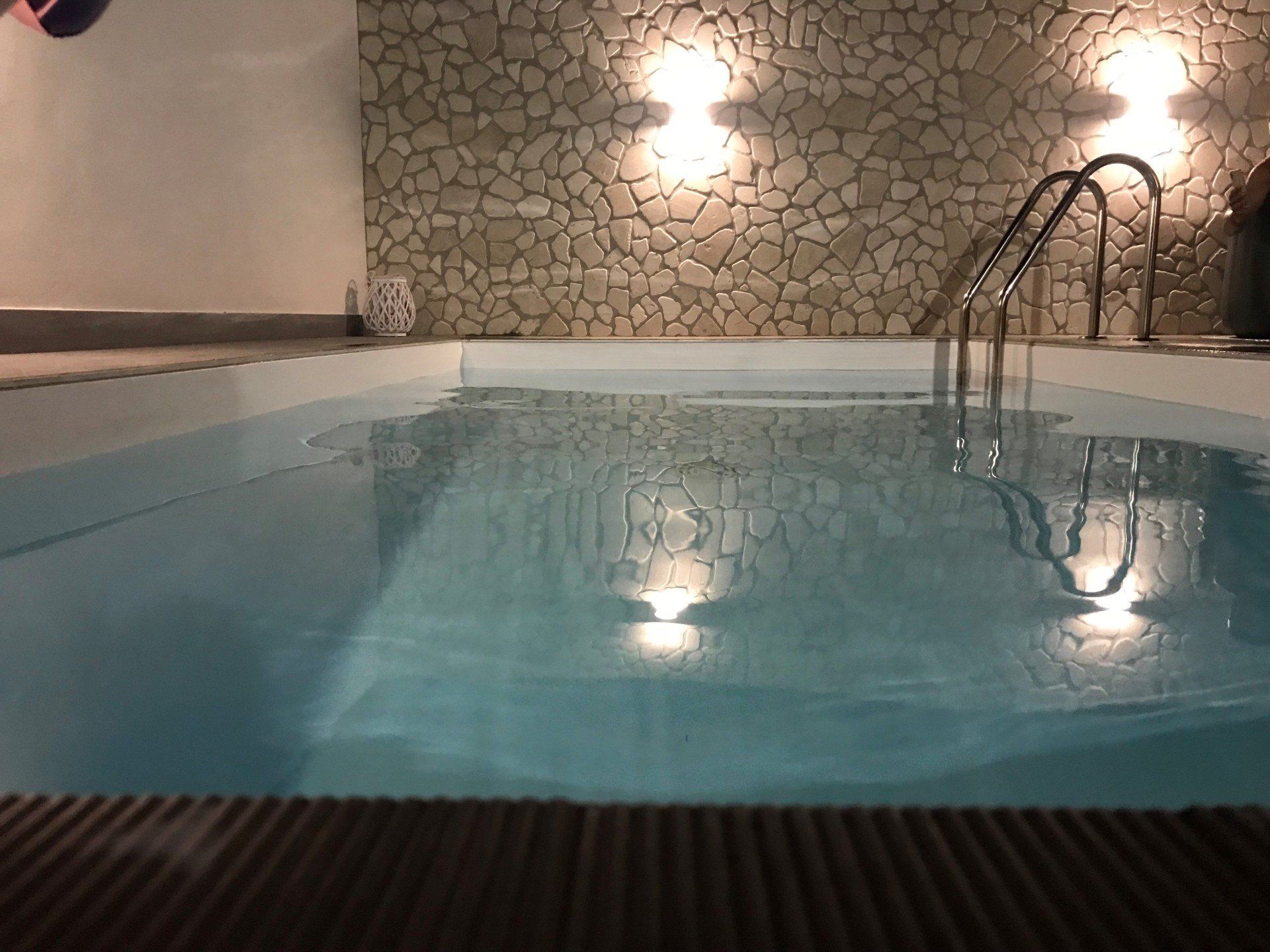 Piscina coperta con muro in pietra e luci sospese che si riflettono sull'acqua.